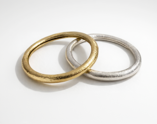 Two bangles, one gold and one silver, on a white background
