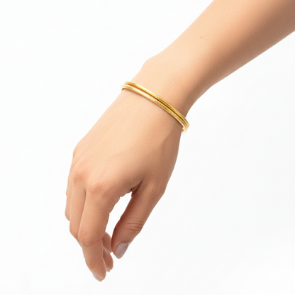 Gold bangles on a hand against a white background