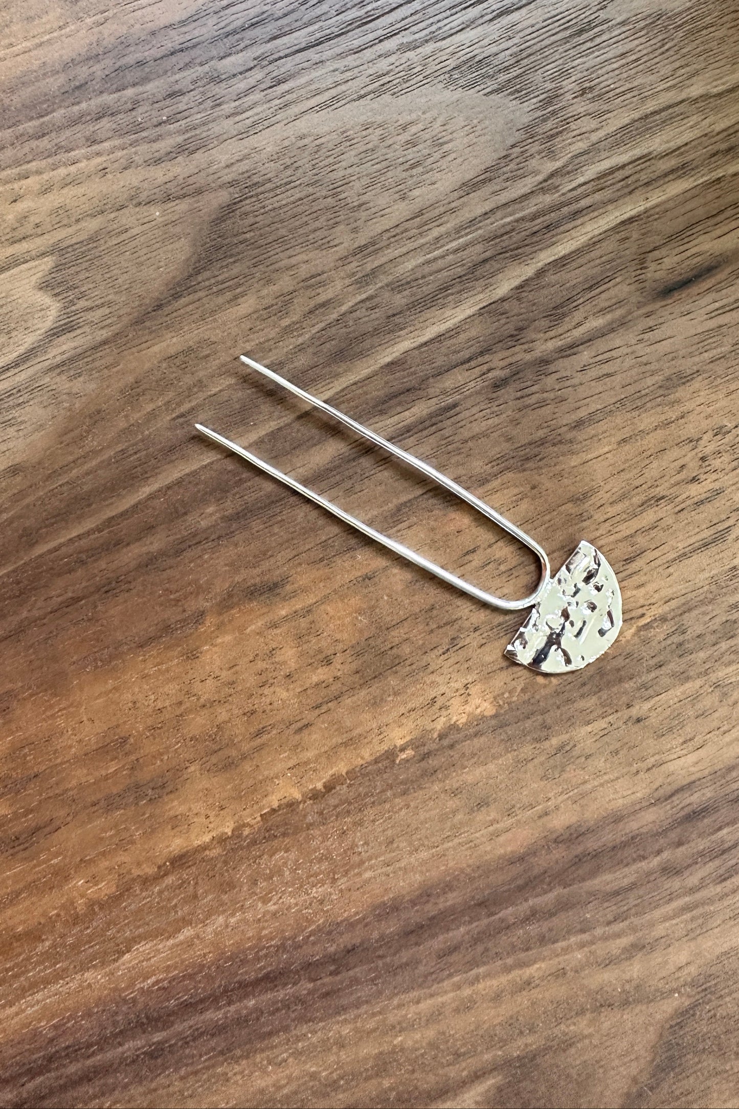 Silver hairpin with decorative top on a wooden surface