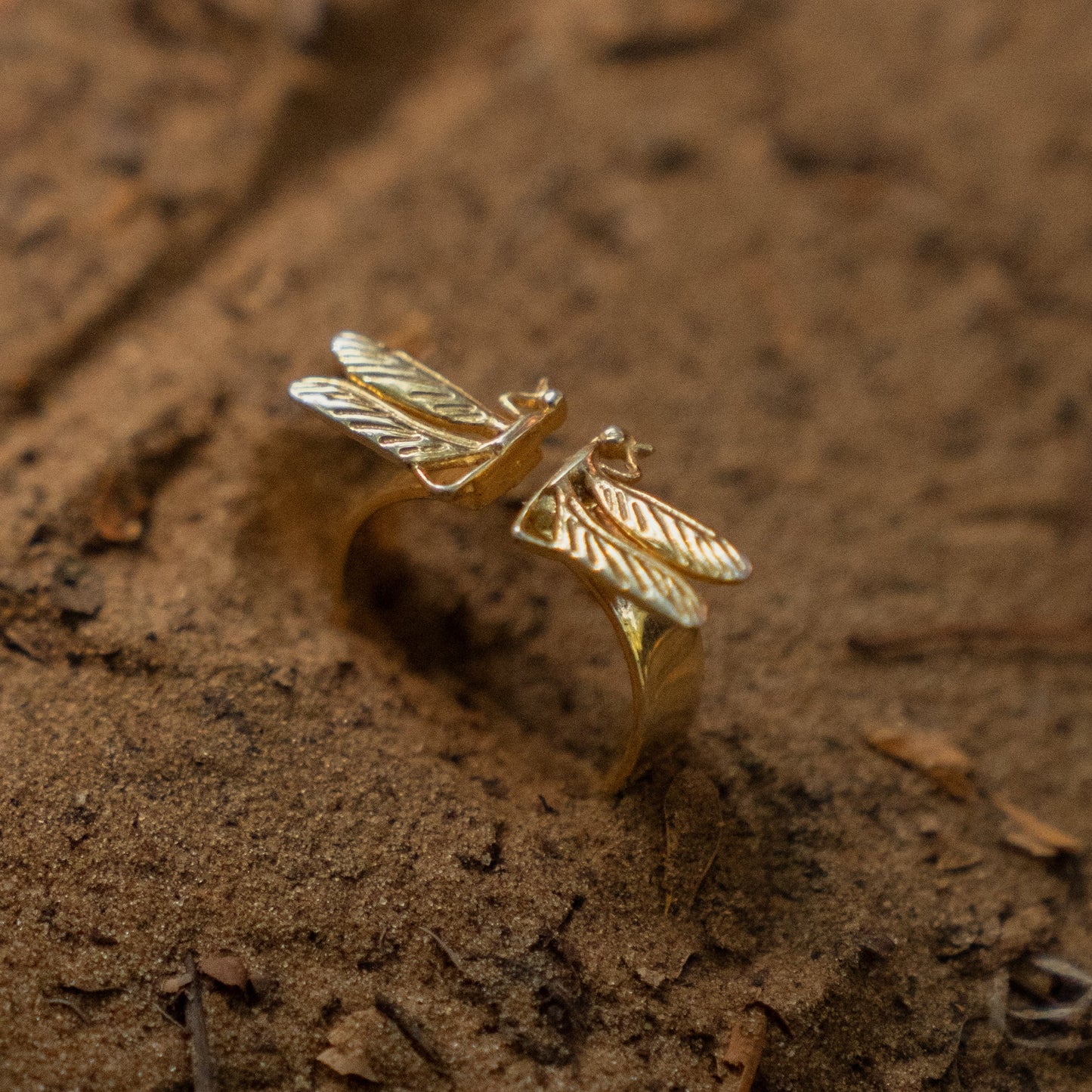 Gold ring with dragonfly design on a textured brown surface