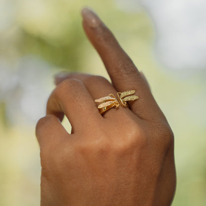 Hand wearing a gold dragonfly ring with a blurred natural background