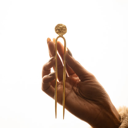 Hand holding a gold hair clip against a white background