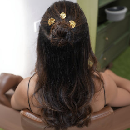 Close-up of a person's hair styled with braids and gold hair accessories on a blurred background