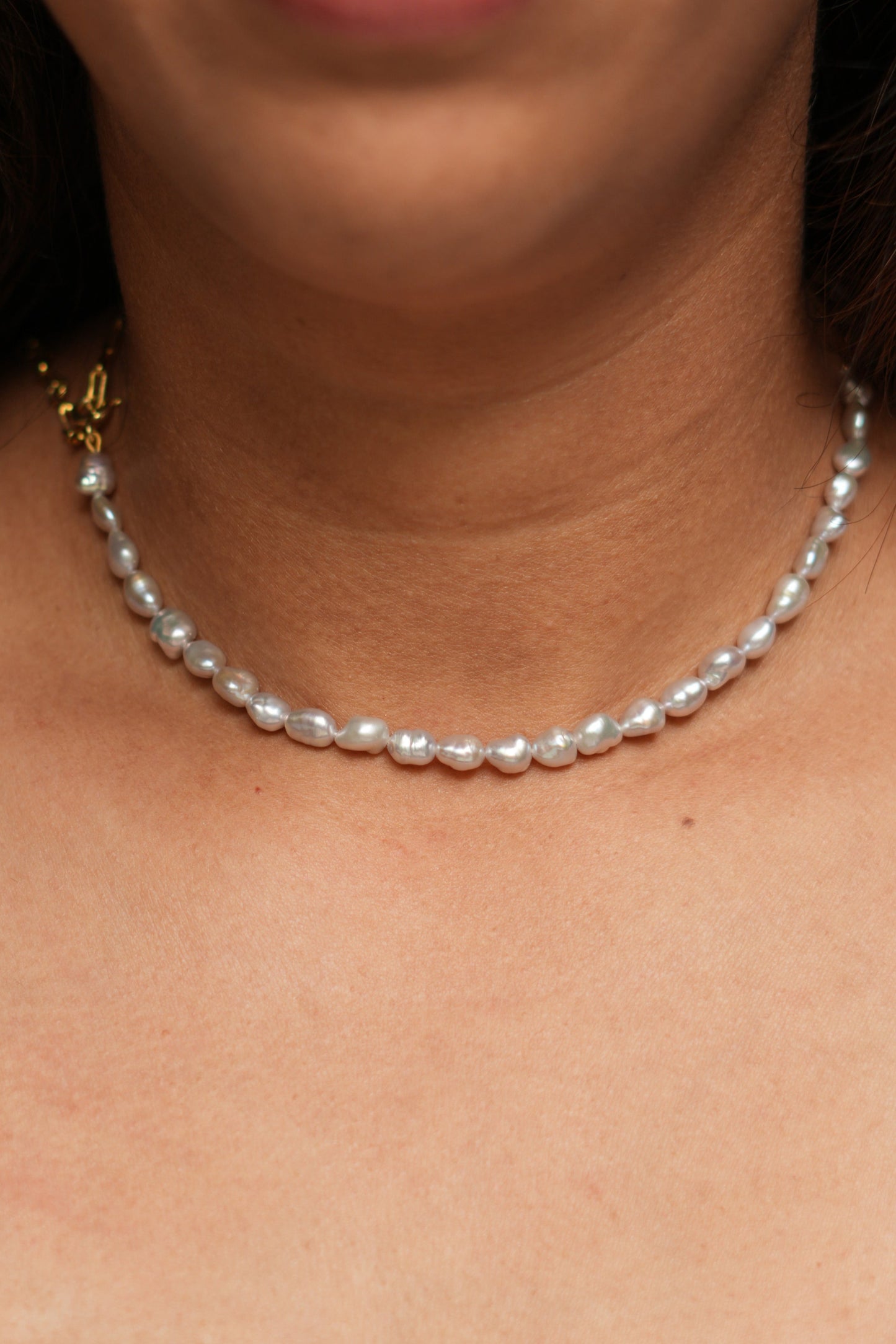 A person wearing a sterling silver and 18kt gold plated half and half pearl necklace with a paperclip chain.