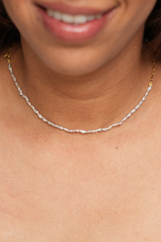 Person wearing a silver necklace with a white top.