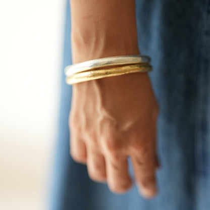 Hand wearing two gold bangles on a blurred blue background
