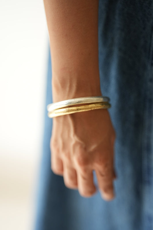 Hand wearing two gold bracelets on a blurred blue background