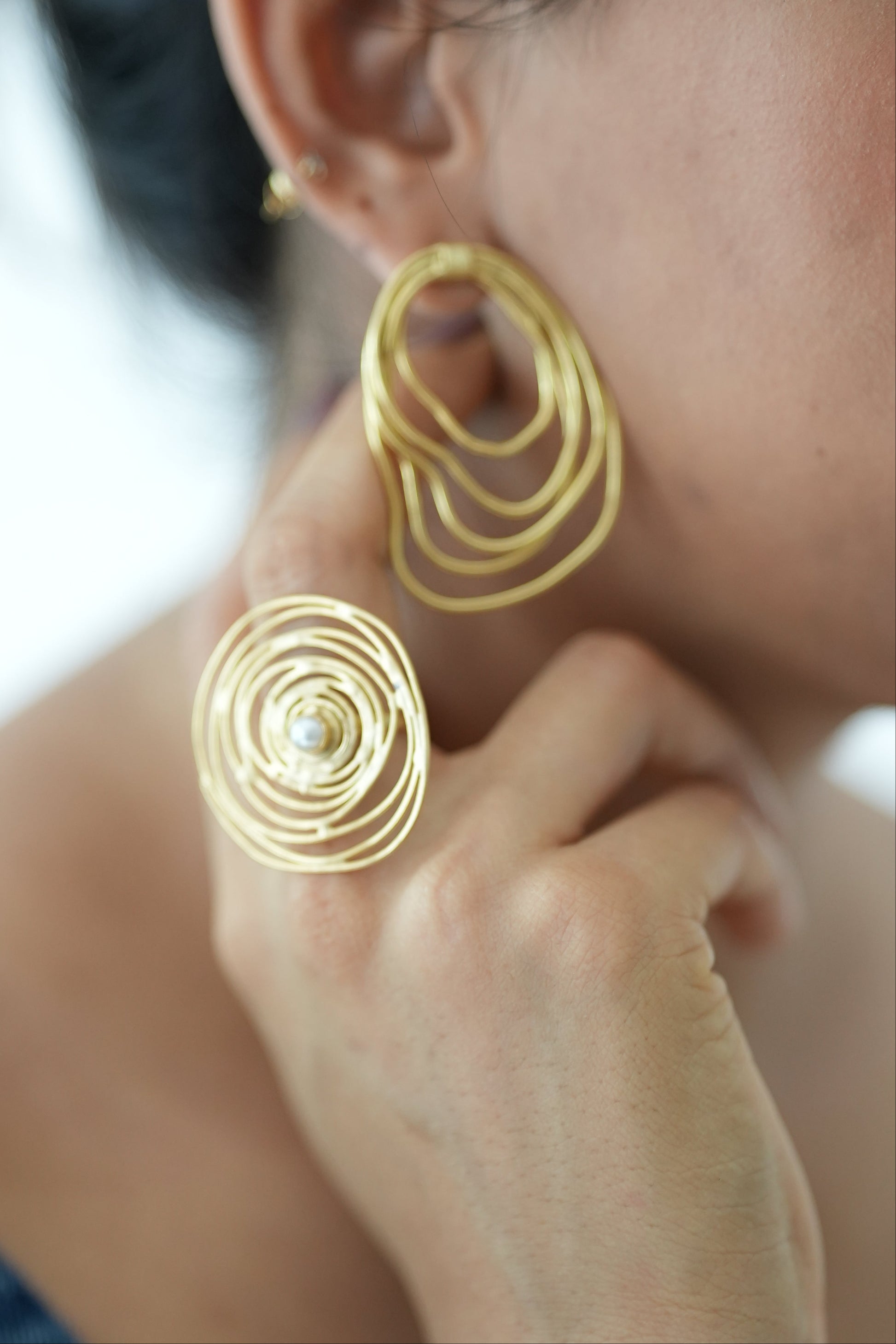 Gold spiral earrings being worn on a person's ear.