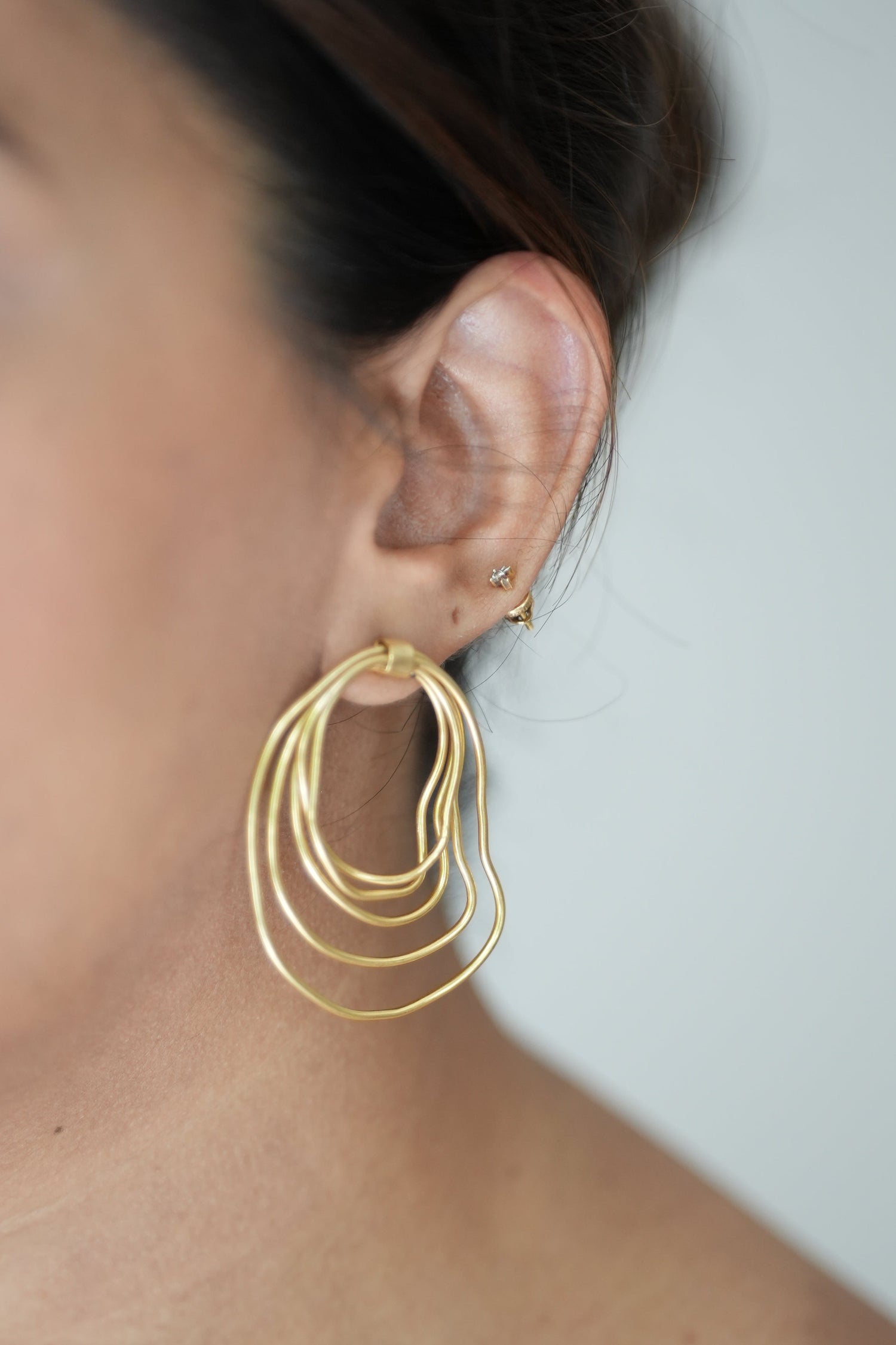 Gold earrings worn by a person against a neutral background