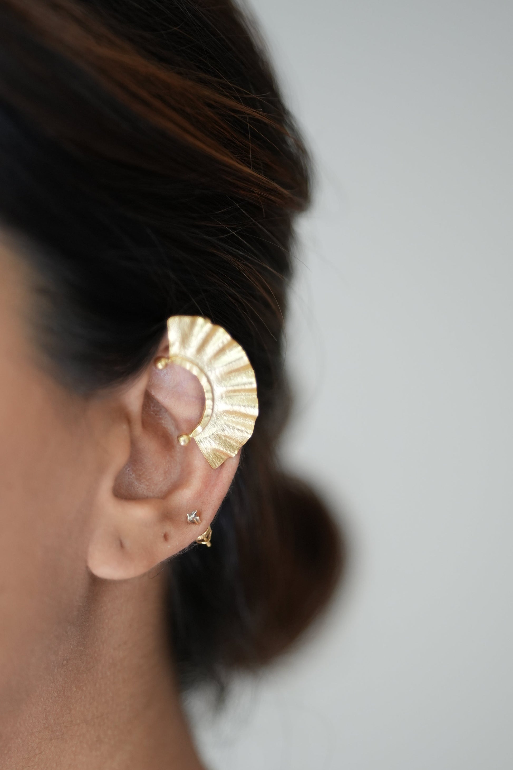 Close-up of a person wearing gold earrings with a neutral background