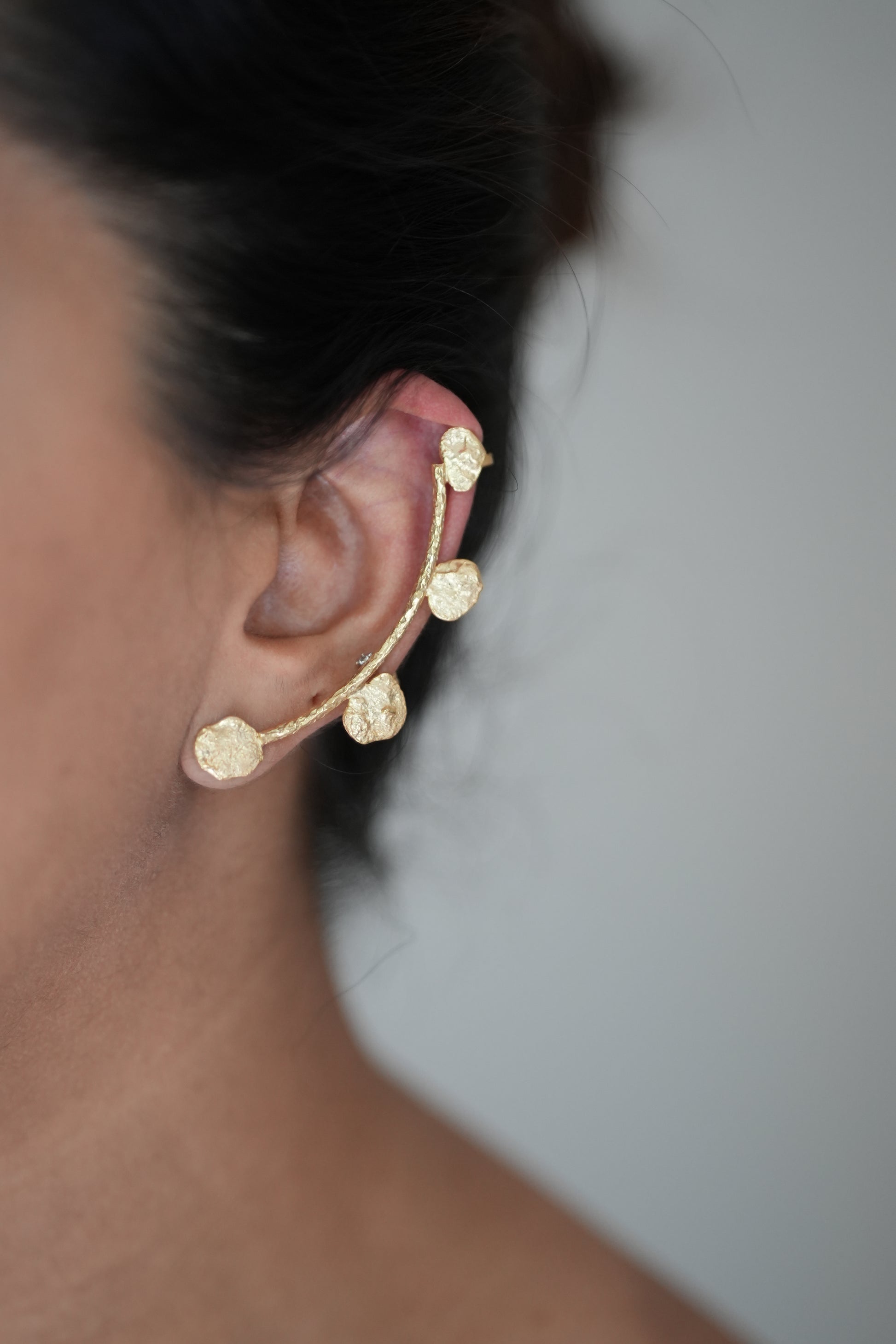 Gold earring worn on an ear with a blurred background