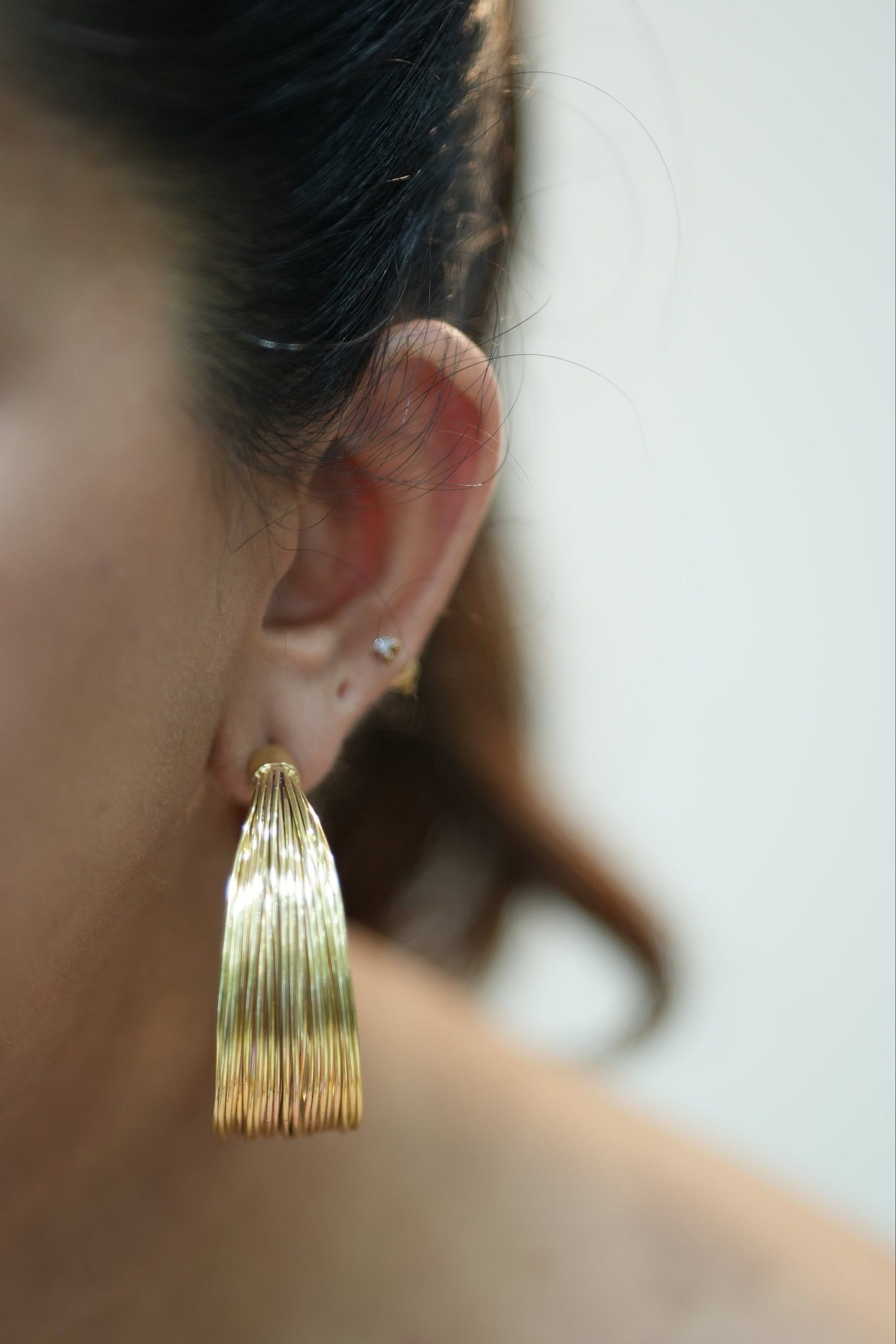 Close-up of a person wearing a gold earring with a blurred background