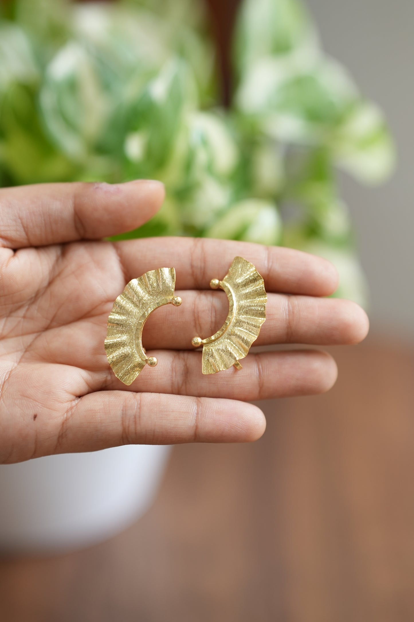 Gold earrings held in a hand with a blurred plant background
