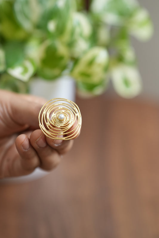 Gold ring with a pearl held by a hand in front of a blurred green plant