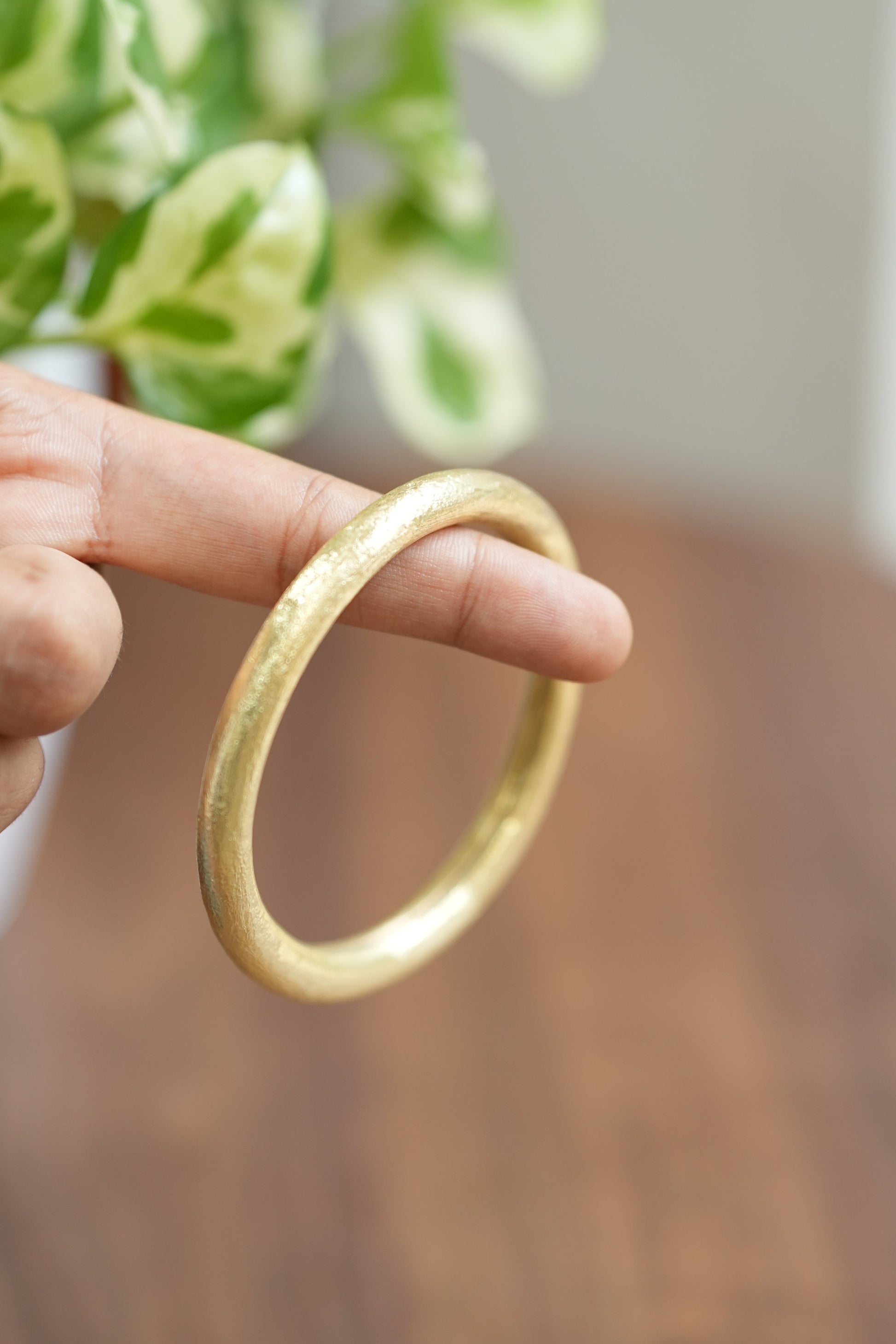 Gold bracelet held by a hand with a blurred background