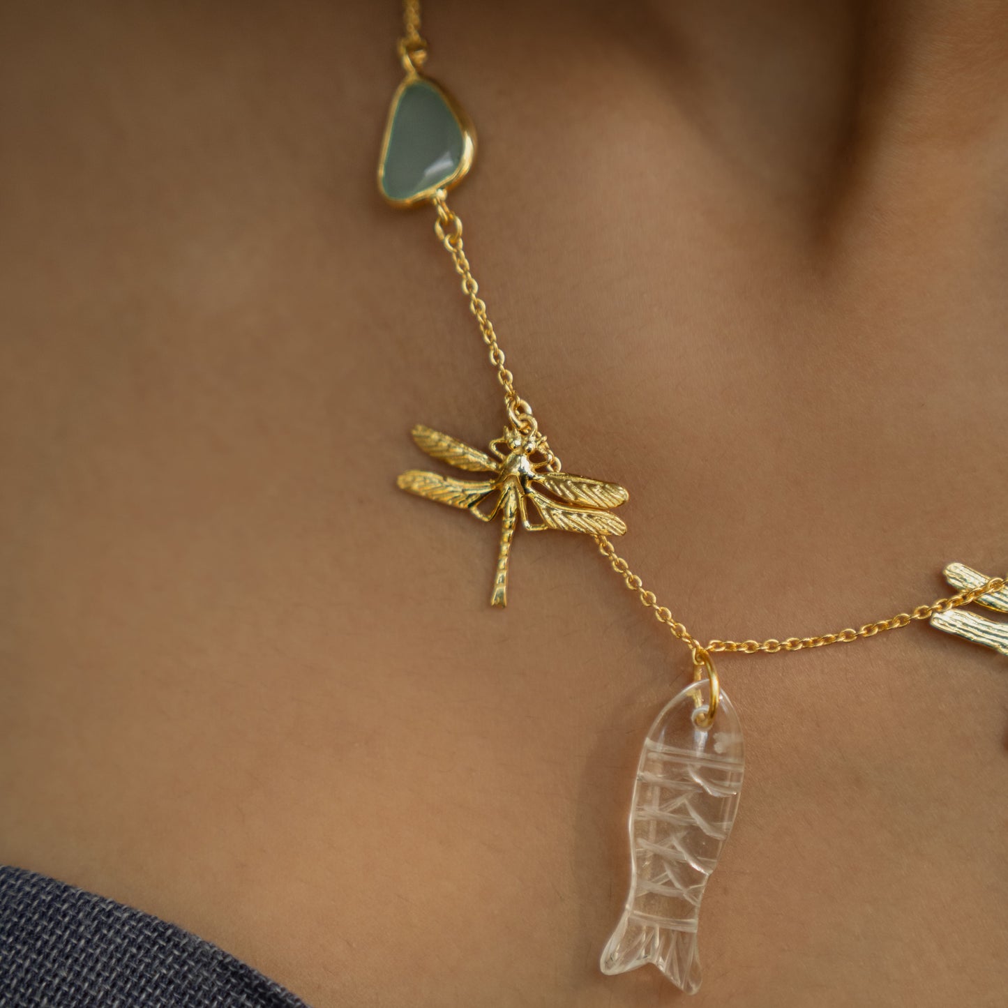 Gold necklace with dragonfly semi precious stone pendants on a blurred background