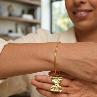 Woman wearing a gold bracelet and ring, with a blurred indoor background