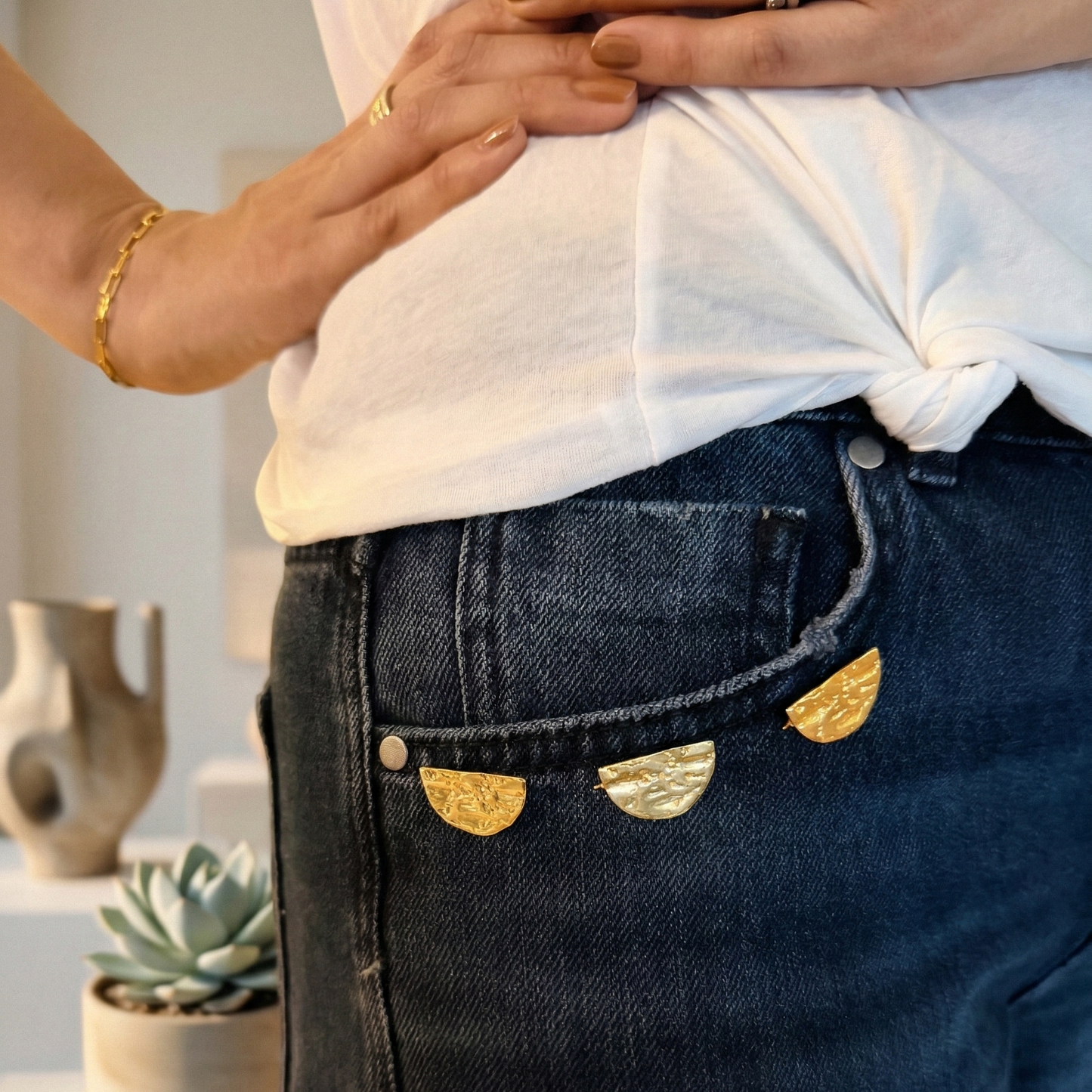 Person wearing dark blue jeans with gold decorative brooches , standing indoors.
