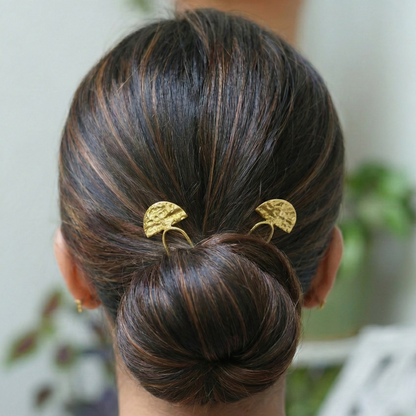 Person with a styled hair bun wearing gold hair accessories, with a blurred indoor background.
