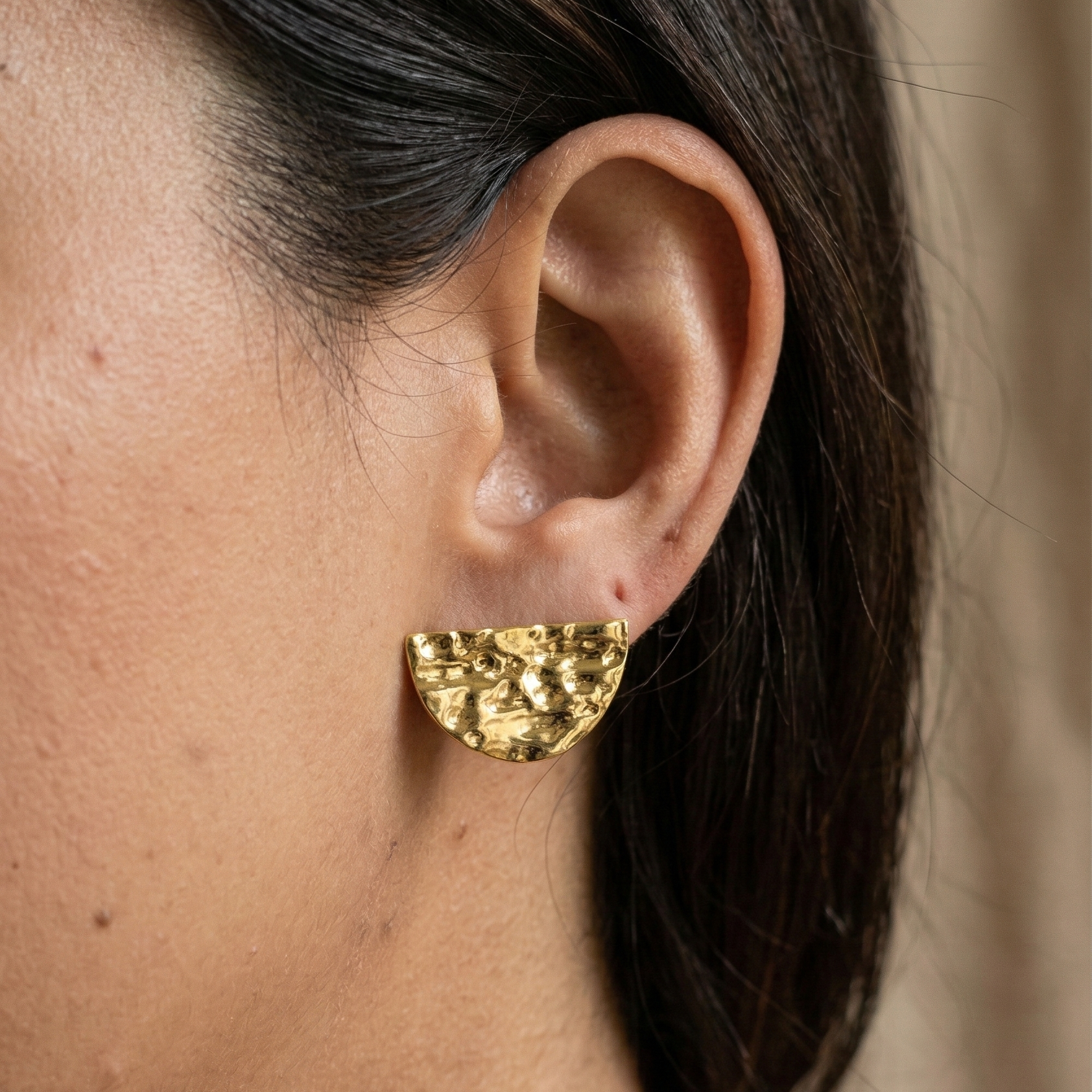 Gold earring worn by a person with a neutral background
