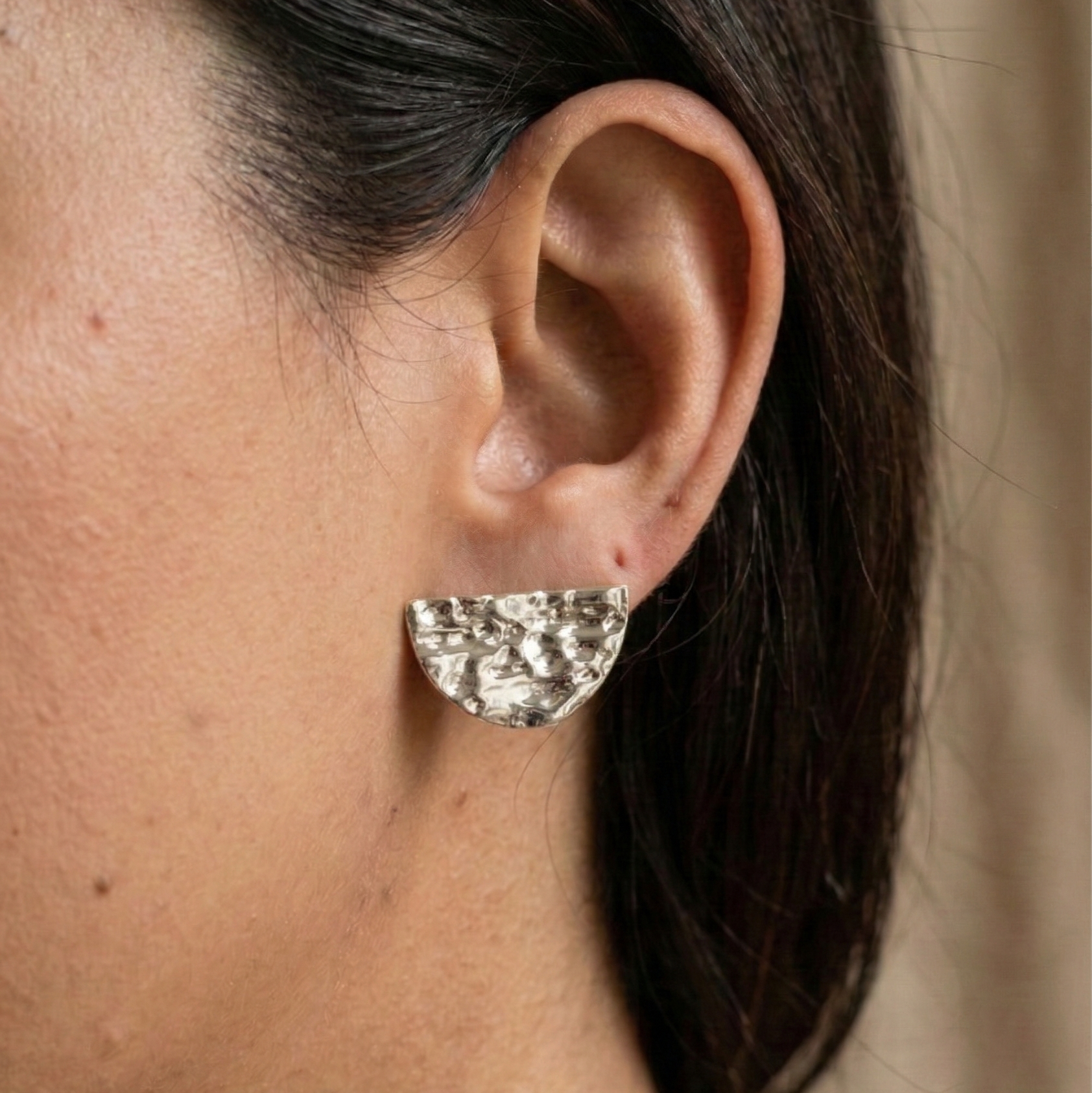 Silver earring worn by a person with dark hair against a neutral background