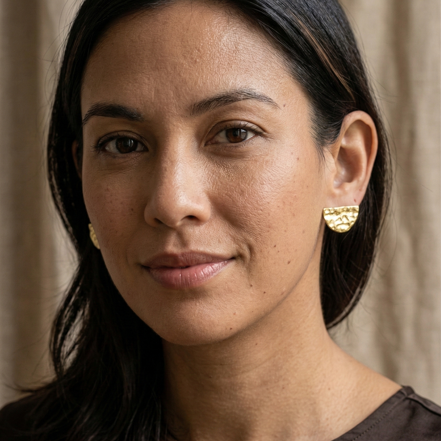 Woman wearing gold earrings against a neutral background