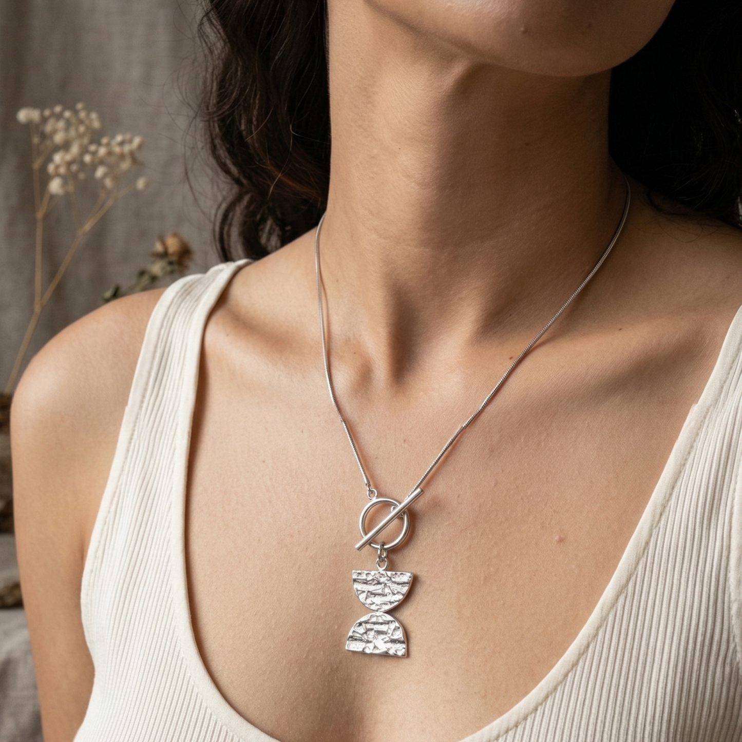 Woman wearing a necklace with a Double D pendant against a neutral background