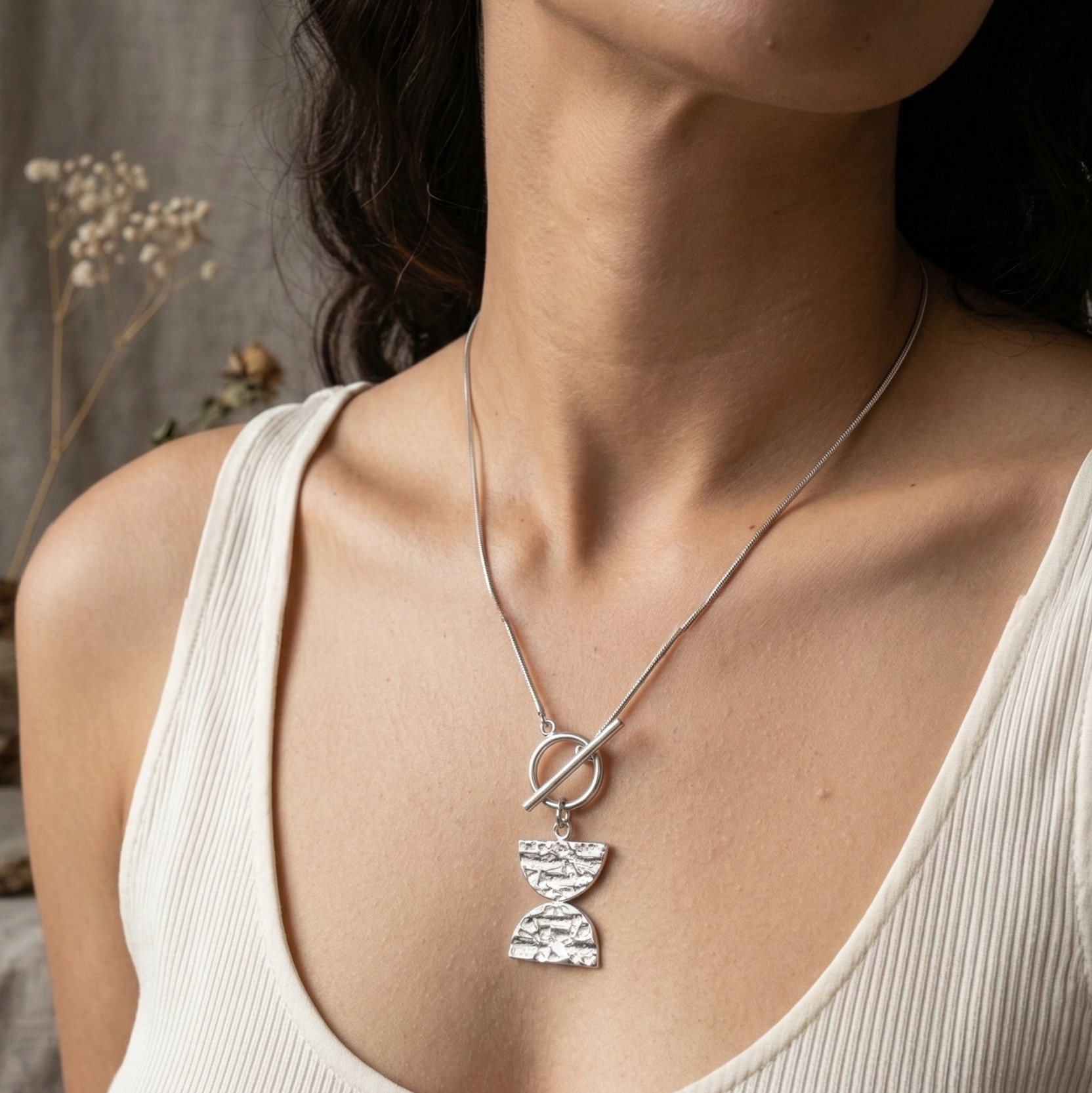 Woman wearing a necklace with a Double D pendant against a neutral background