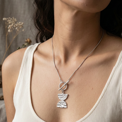 Woman wearing a necklace with a Double D pendant against a neutral background