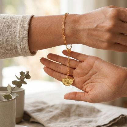 Person wearing a gold bracelet with a D textured charm on a neutral background