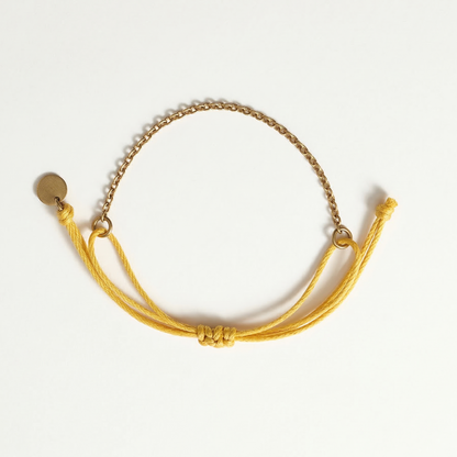 Gold bracelet with a chain and yellow cord on a white background