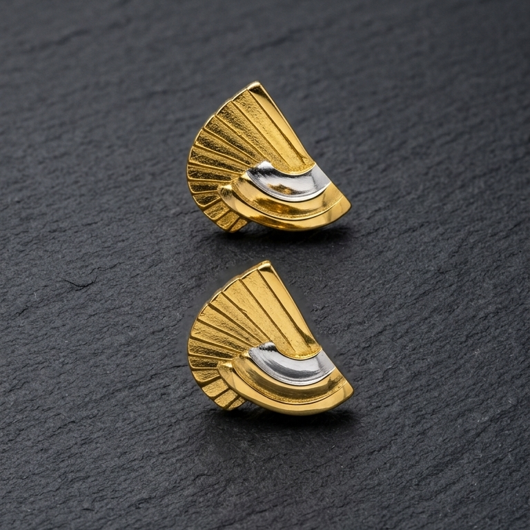 A pair of gold fan-shaped stud cuff links with a curved silver inlay, displayed on a dark textured slate surface.