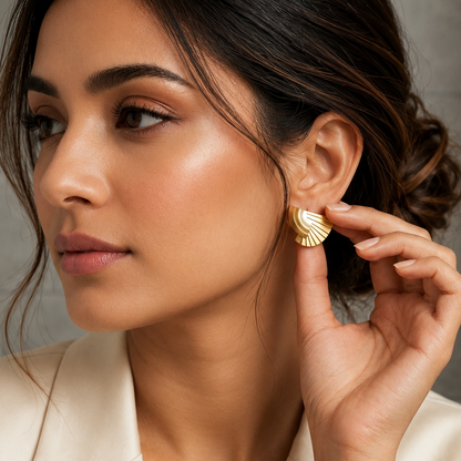 A woman in a cream blazer wearing a gold crescent-shaped stud earring, shown in a close-up profile view against a soft gray background.
