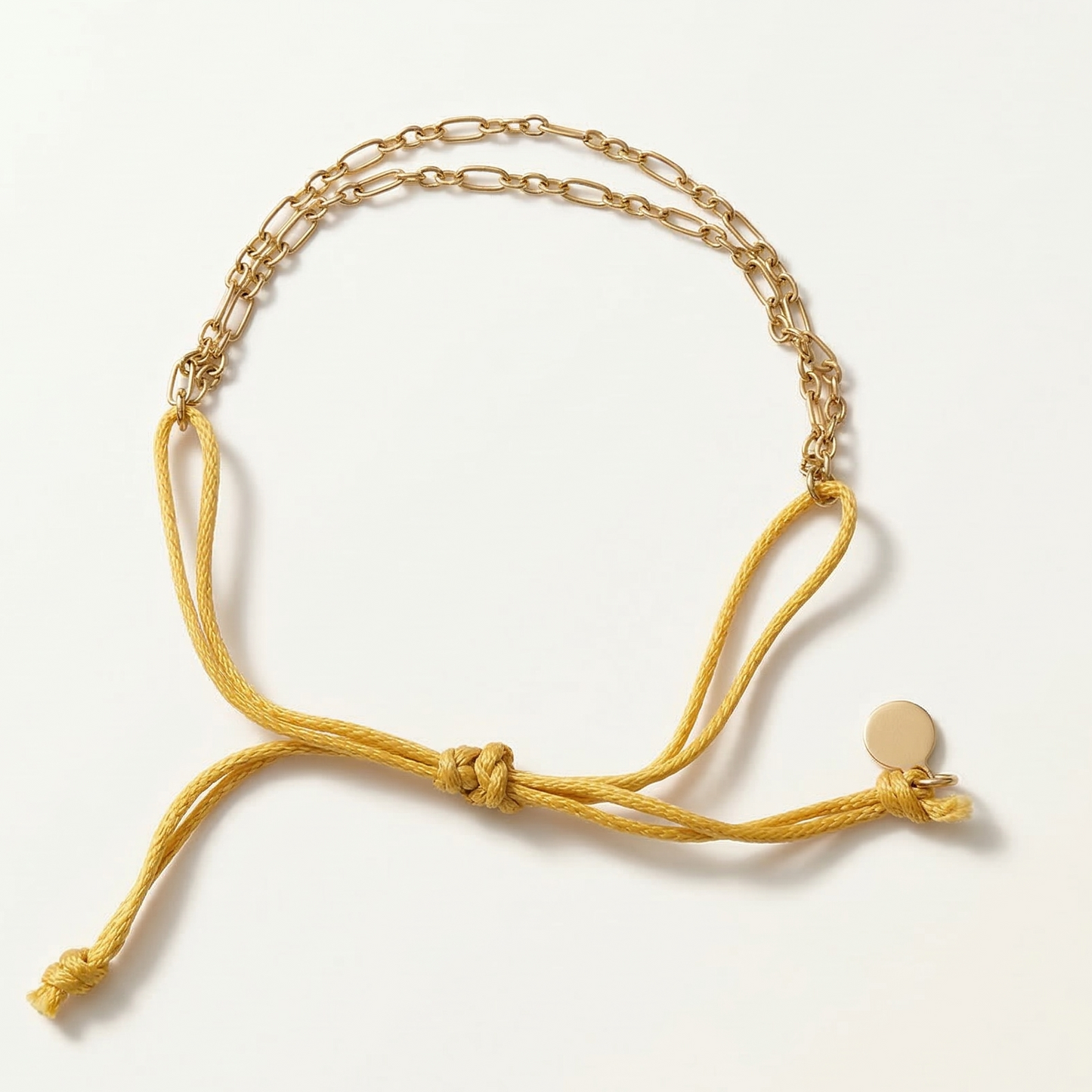 Gold bracelet with a yellow cord on a white background