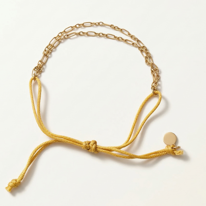 Gold bracelet with a yellow cord on a white background
