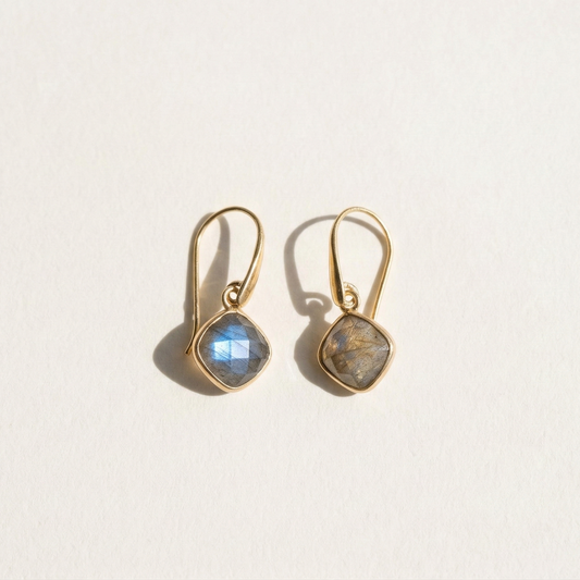 Gold earrings with labradorite semi-precious stones on a light beige background