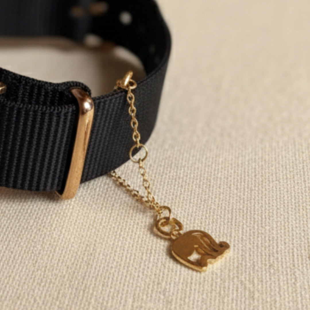 Black watch with a gold chain charm on a beige background