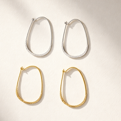 Two pairs of hoop earrings, one gold and one silver, on a light background.