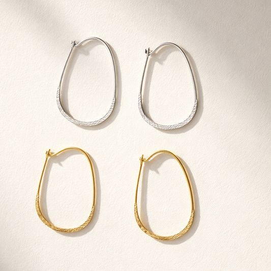 Two pairs of hoop earrings, one gold and one silver, on a light background.