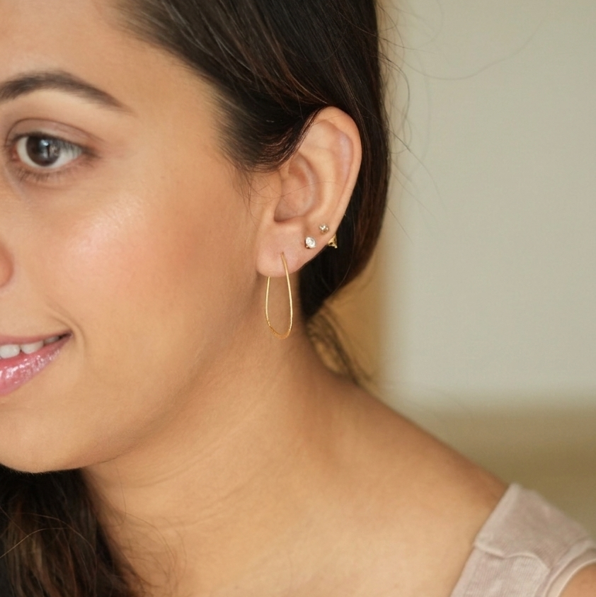 Close-up of a woman wearing gold hoop earrings with a neutral background