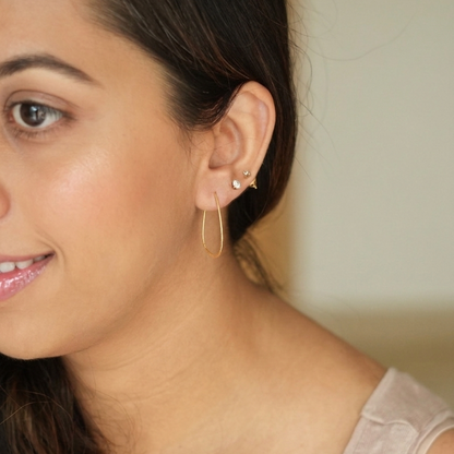 Close-up of a woman wearing gold hoop earrings with a neutral background