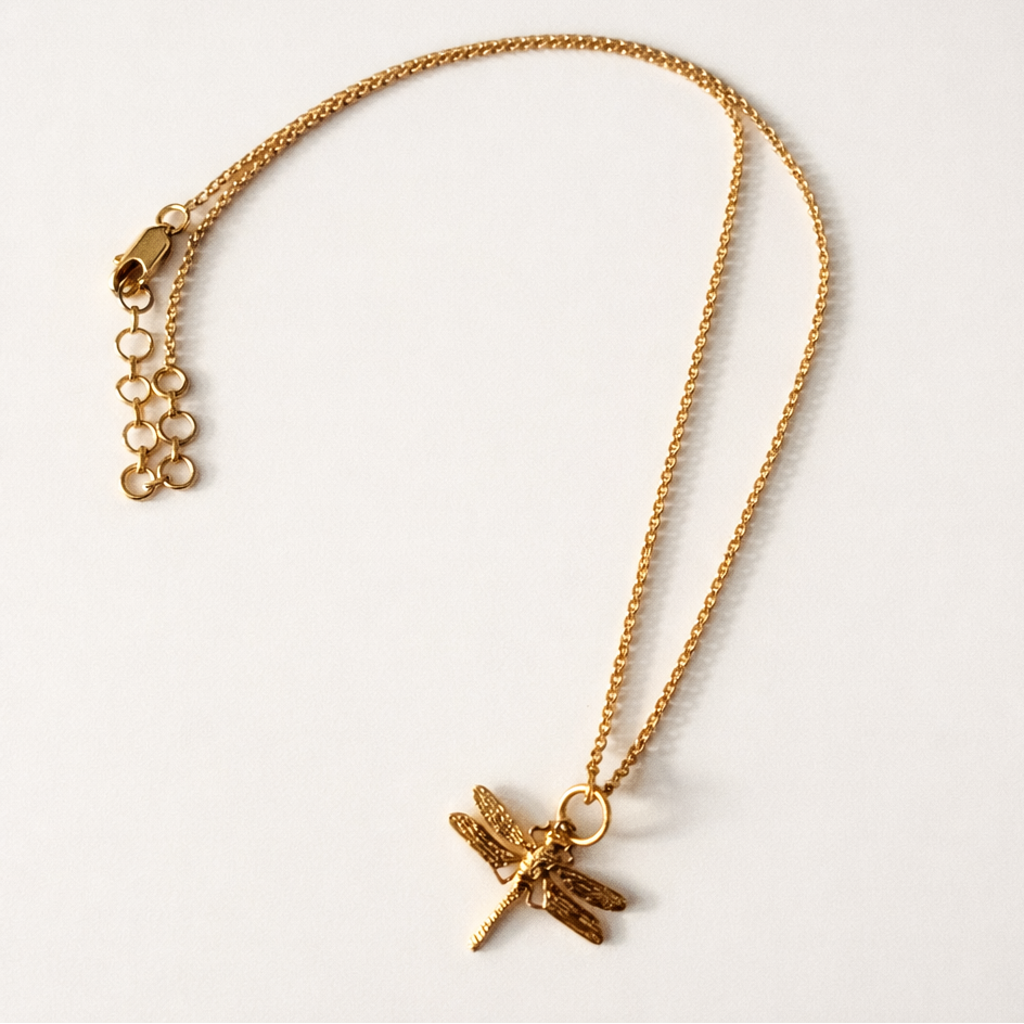 Gold necklace with a dragonfly pendant on a light gray background
