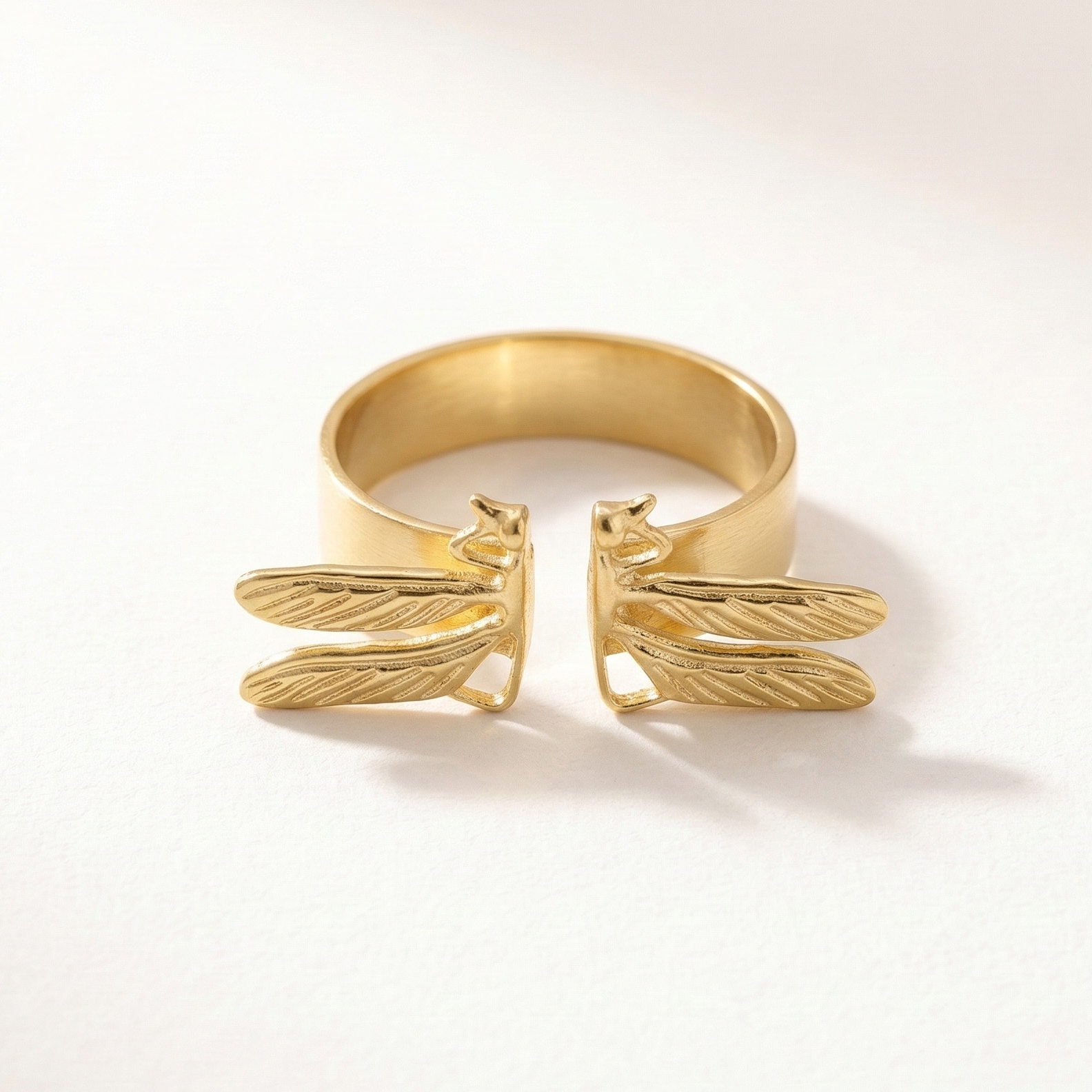 Gold ring with dragonfly design on a light beige background