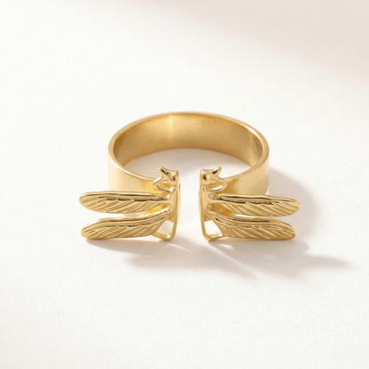 Gold ring with dragonfly design on a light beige background
