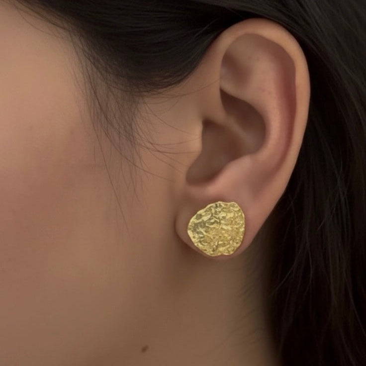 Close-up of a person wearing a gold earring with a textured design.