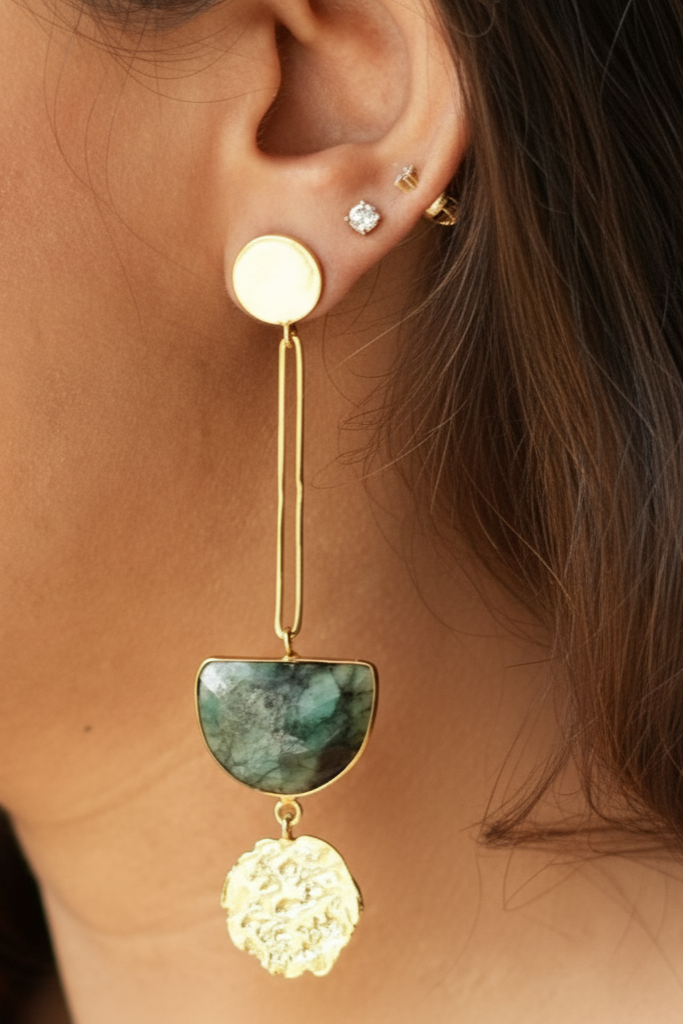 Close-up of an ear with gold earrings featuring a green stone and floral design.
