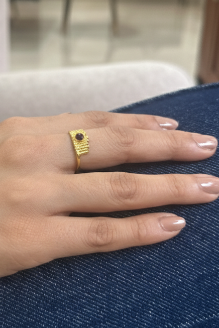 Hand wearing a gold ring with a small yellow object on a blue surface