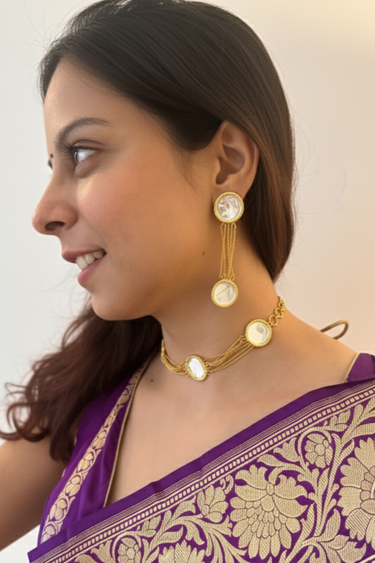 Woman wearing a purple saree with gold patterns, gold jewelry, and holding white flowers.