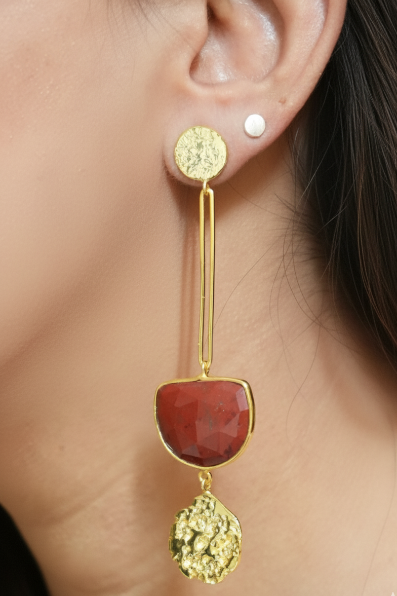 Gold earring with red stone and green gemstone worn by a person