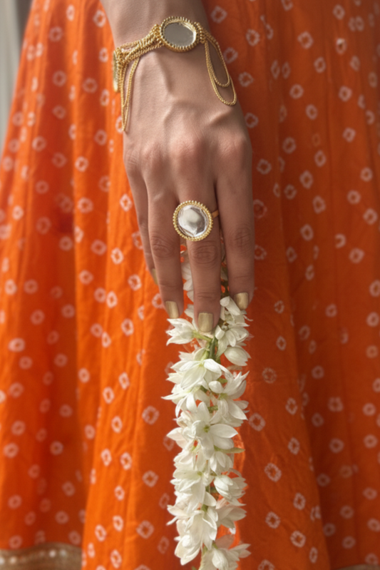 Person wearing an orange traditional outfit with a gold bracelet and ring, holding a white flower garland.